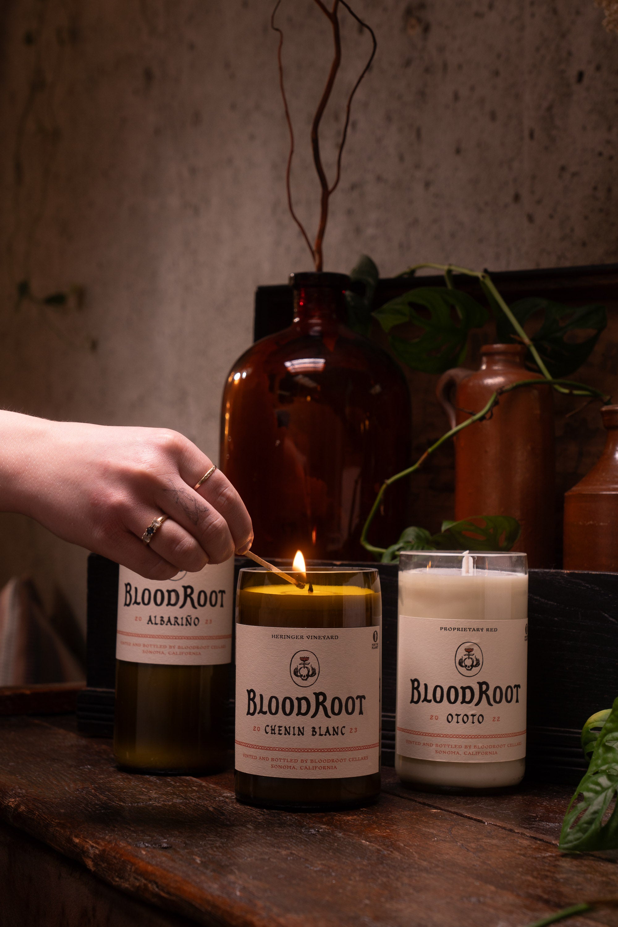 Group of BloodRoot candles in recycled wine bottles being lit on table