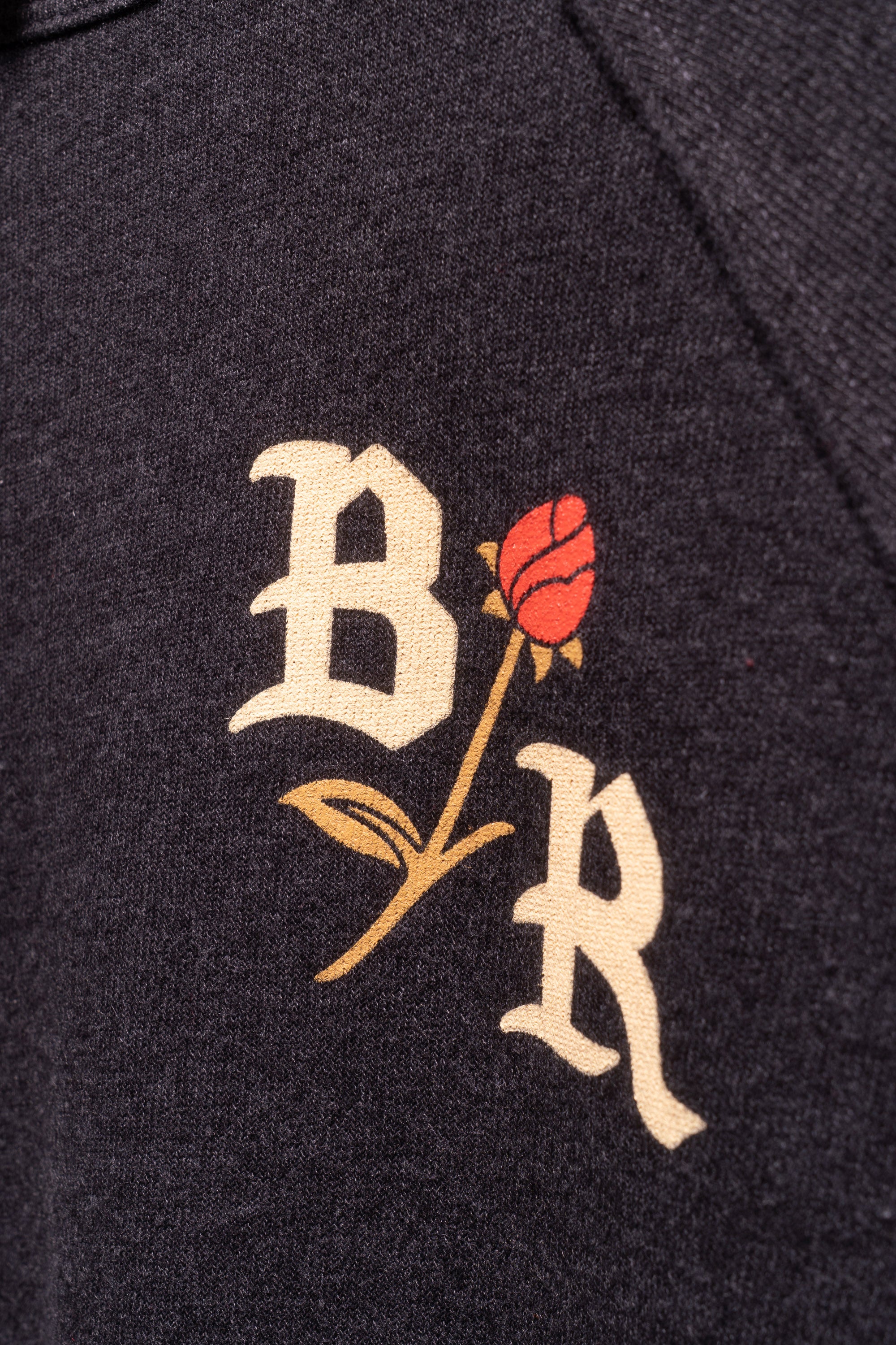 Close up of BR with Rose featured on the front of dark gray crew neck sweatshirt