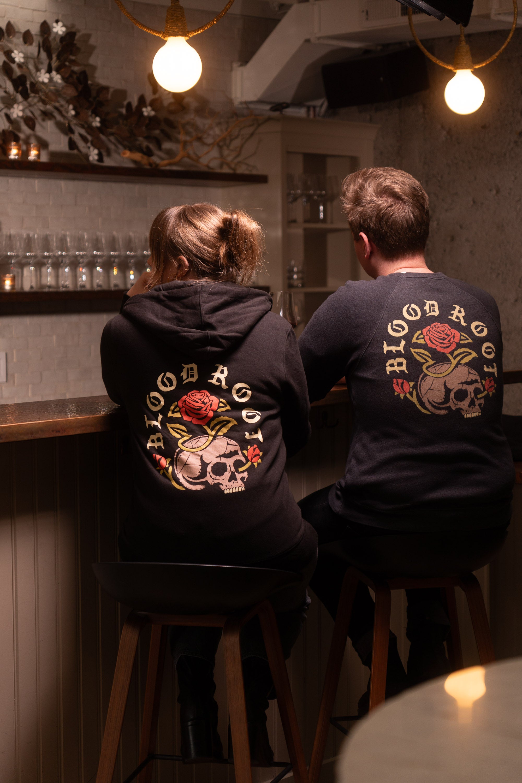A man and woman sit side by side at the bar wearing BloodRoot sweatshirts