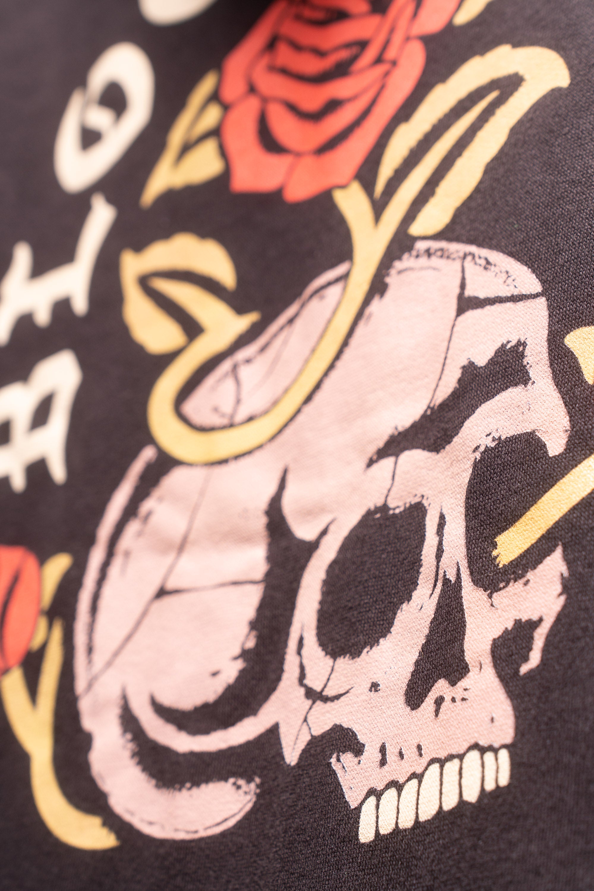 Close up view of skull with roses surrounding featured on the back of black hoodie