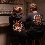 A man and woman sit side by side at the bar wearing BloodRoot sweatshirts